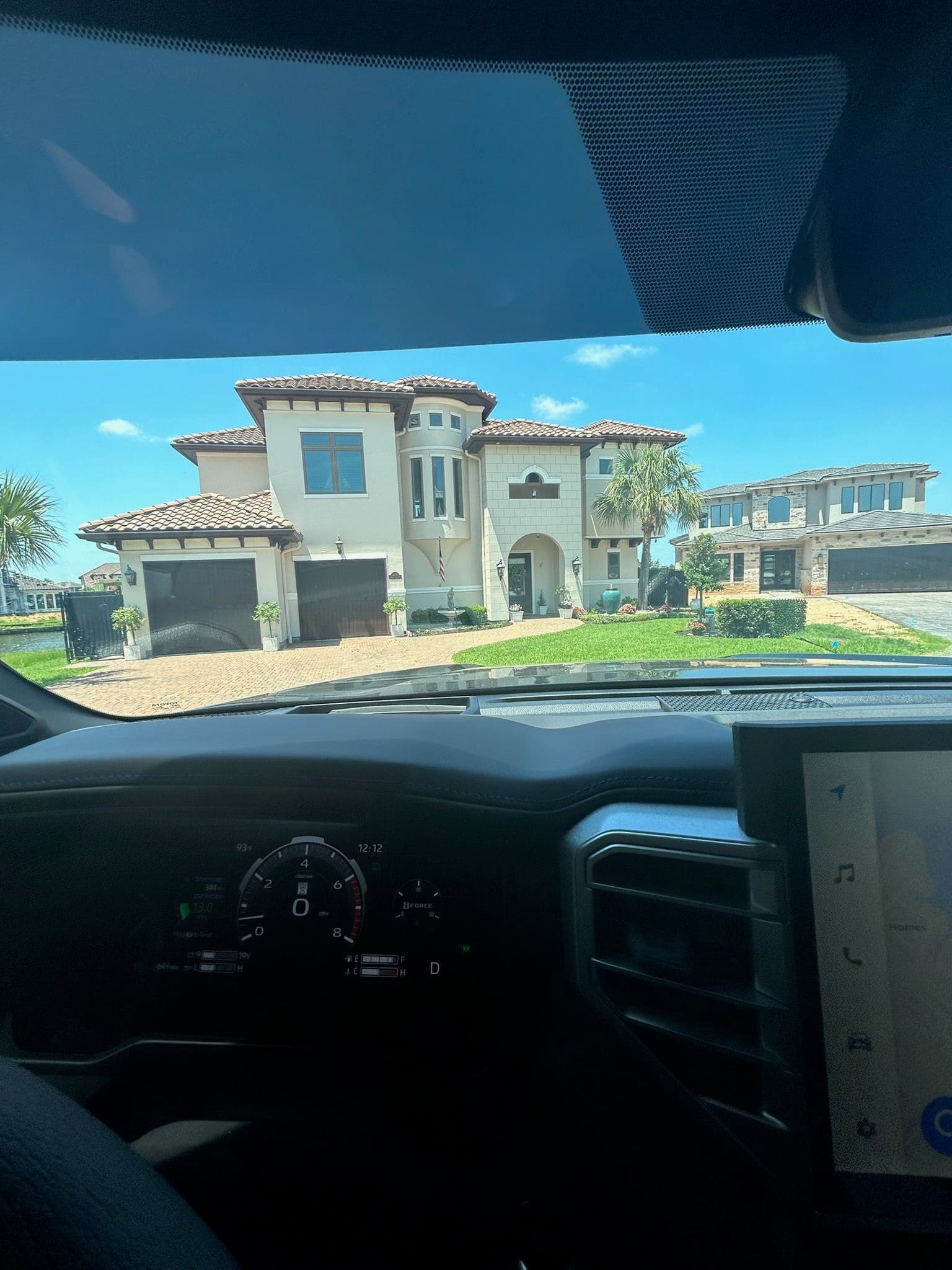 Luxury Mediterranean-style home with palm trees, viewed from a car dashboard.
