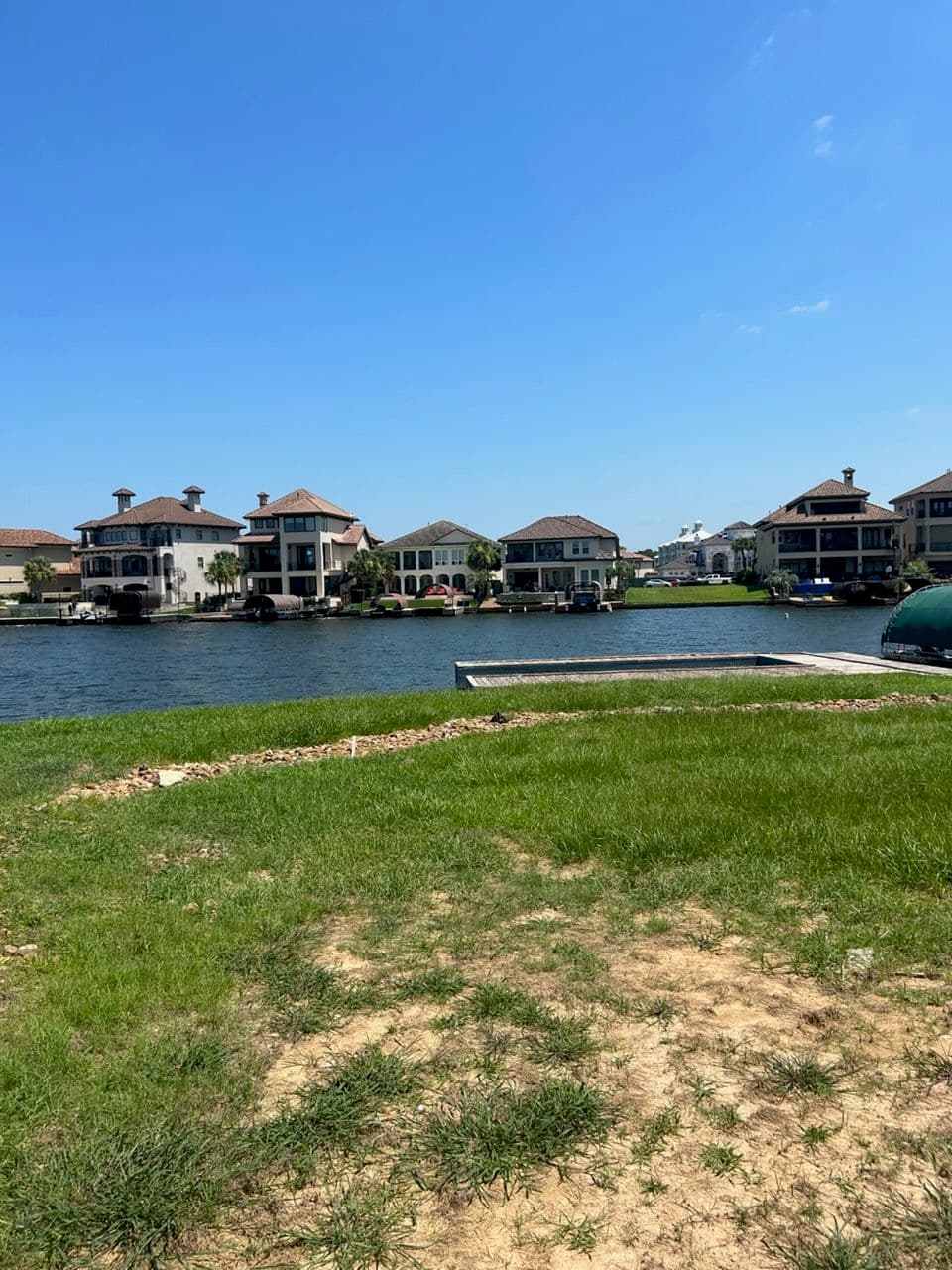 Lakeside view of luxury homes with green grass and clear blue sky.